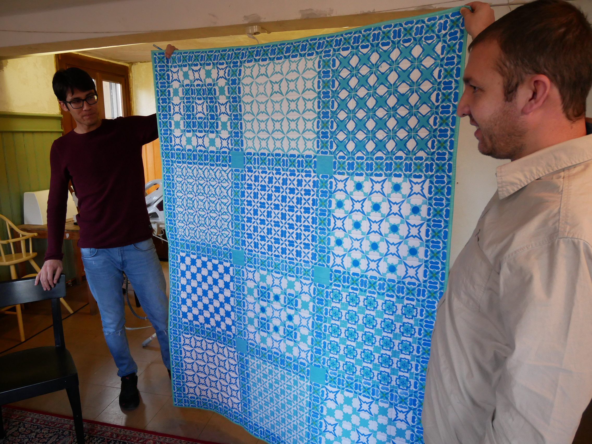 Der Näher Ali (links) hält eine der Decken hoch, die islamische Kunst mit regionaler Handarbeitstechnik verbinden. Samad (rechts) hilft mit, wo er kann.