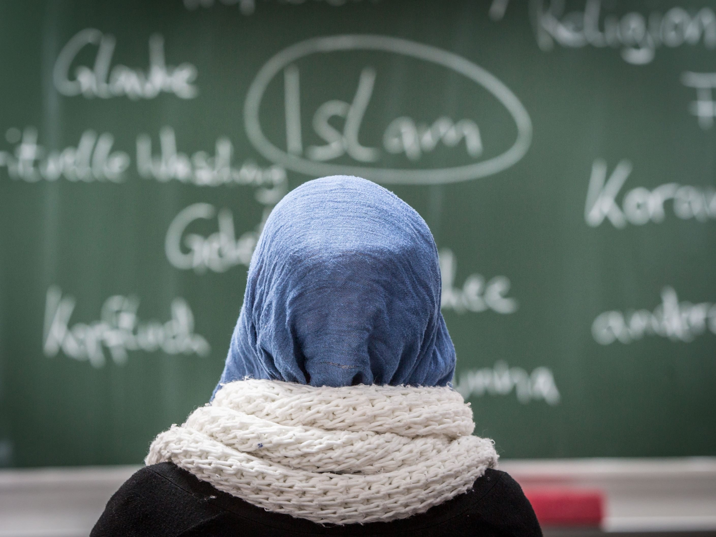 Eine junge Frau mit Kopftuch vor einer Tafel.