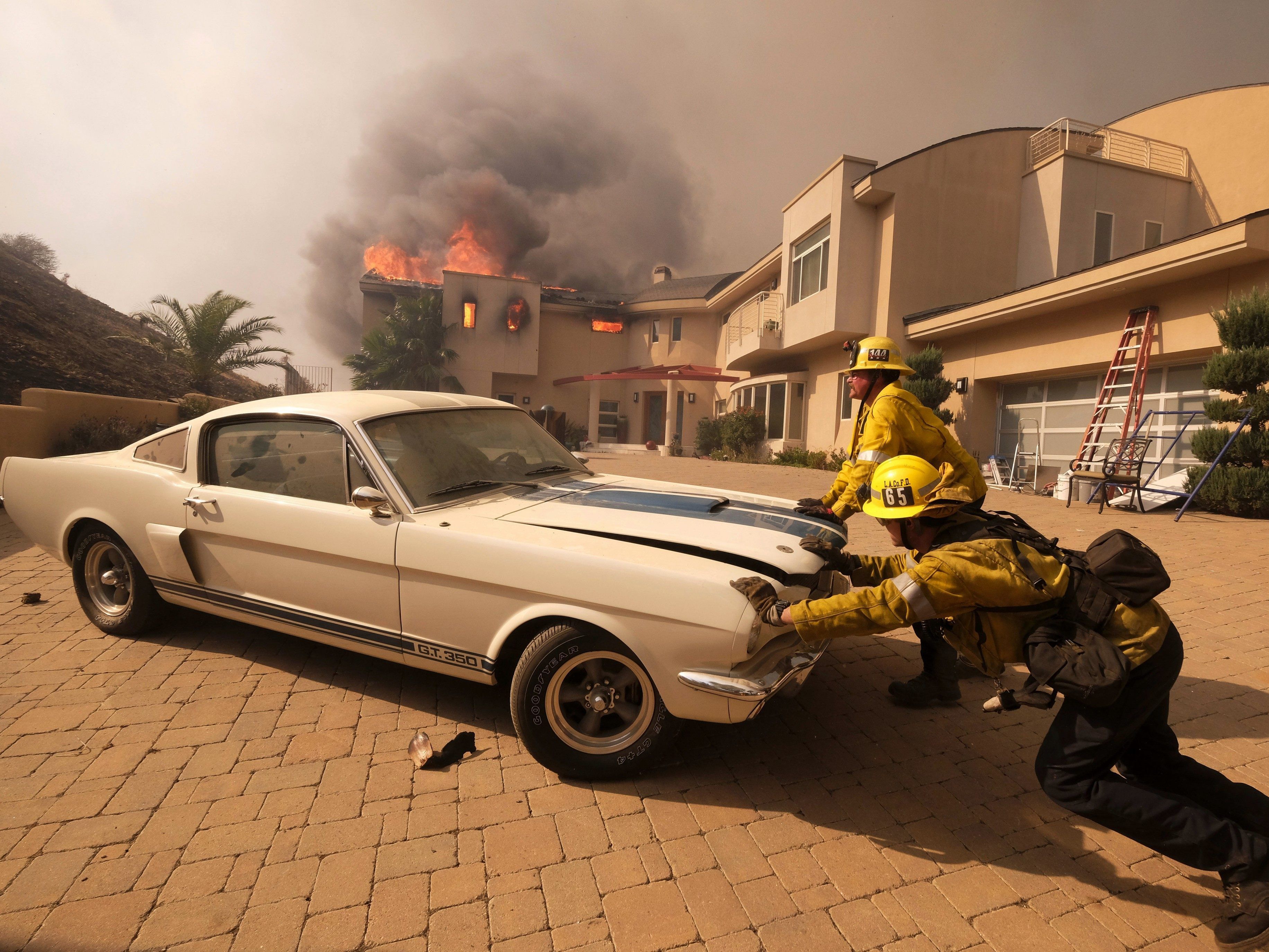 Feuerwehrmänner versuchen ein teures Auto vor dem Flammen in Malibu zu retten.