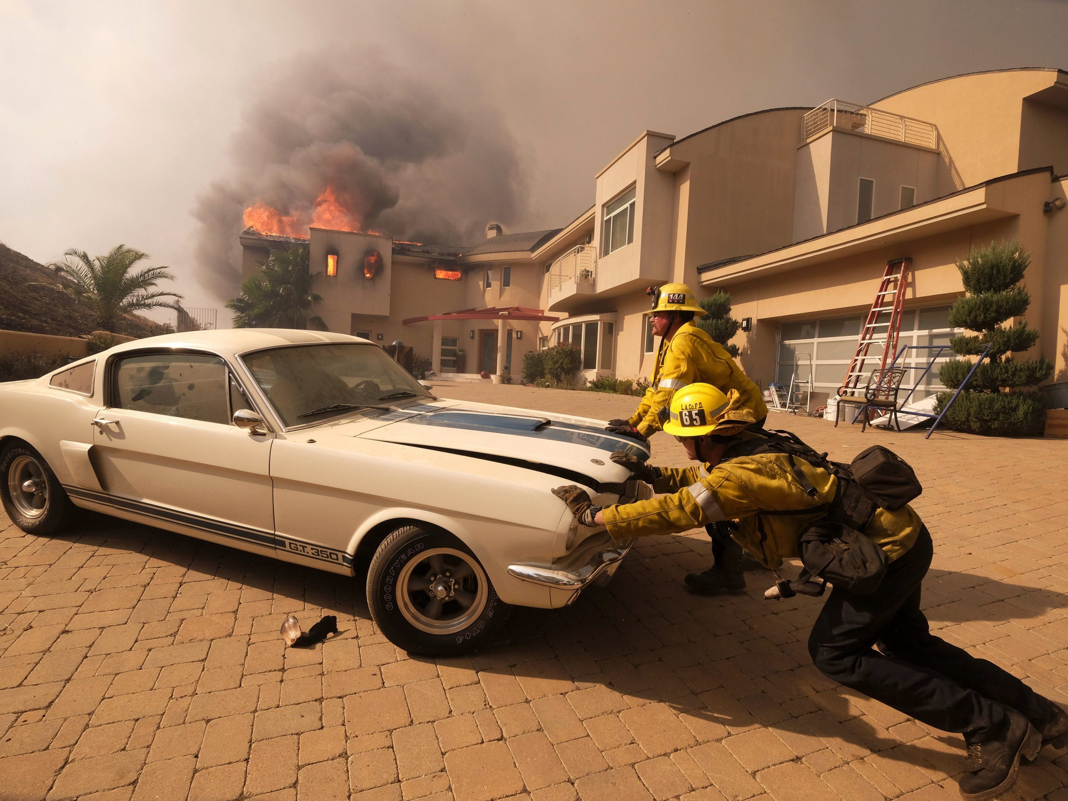 Feuerwehrmänner versuchen ein teures Auto vor dem Flammen in Malibu zu retten.