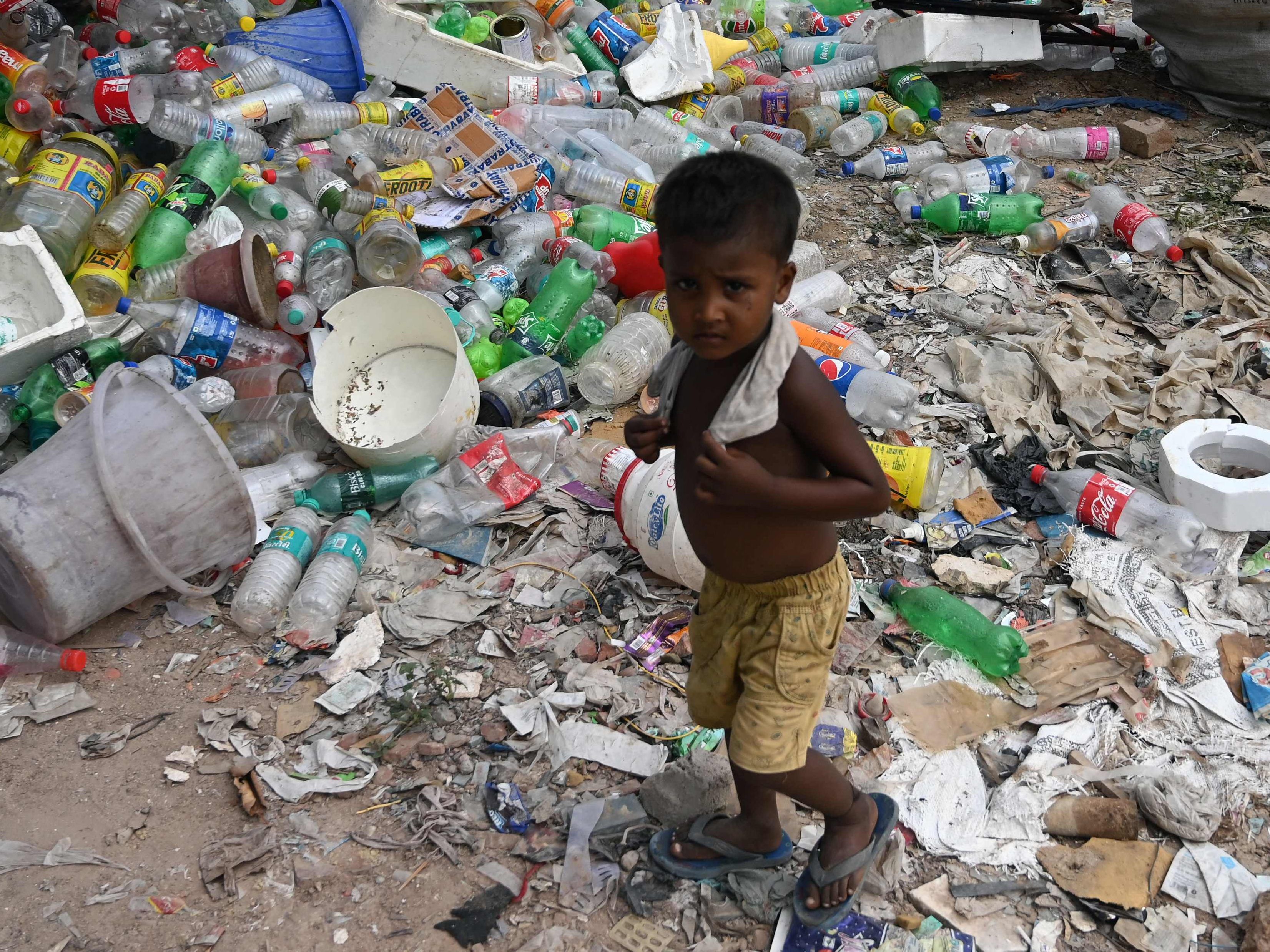 Ein Kind in New Delhi umzingelt von Plastikmüll.