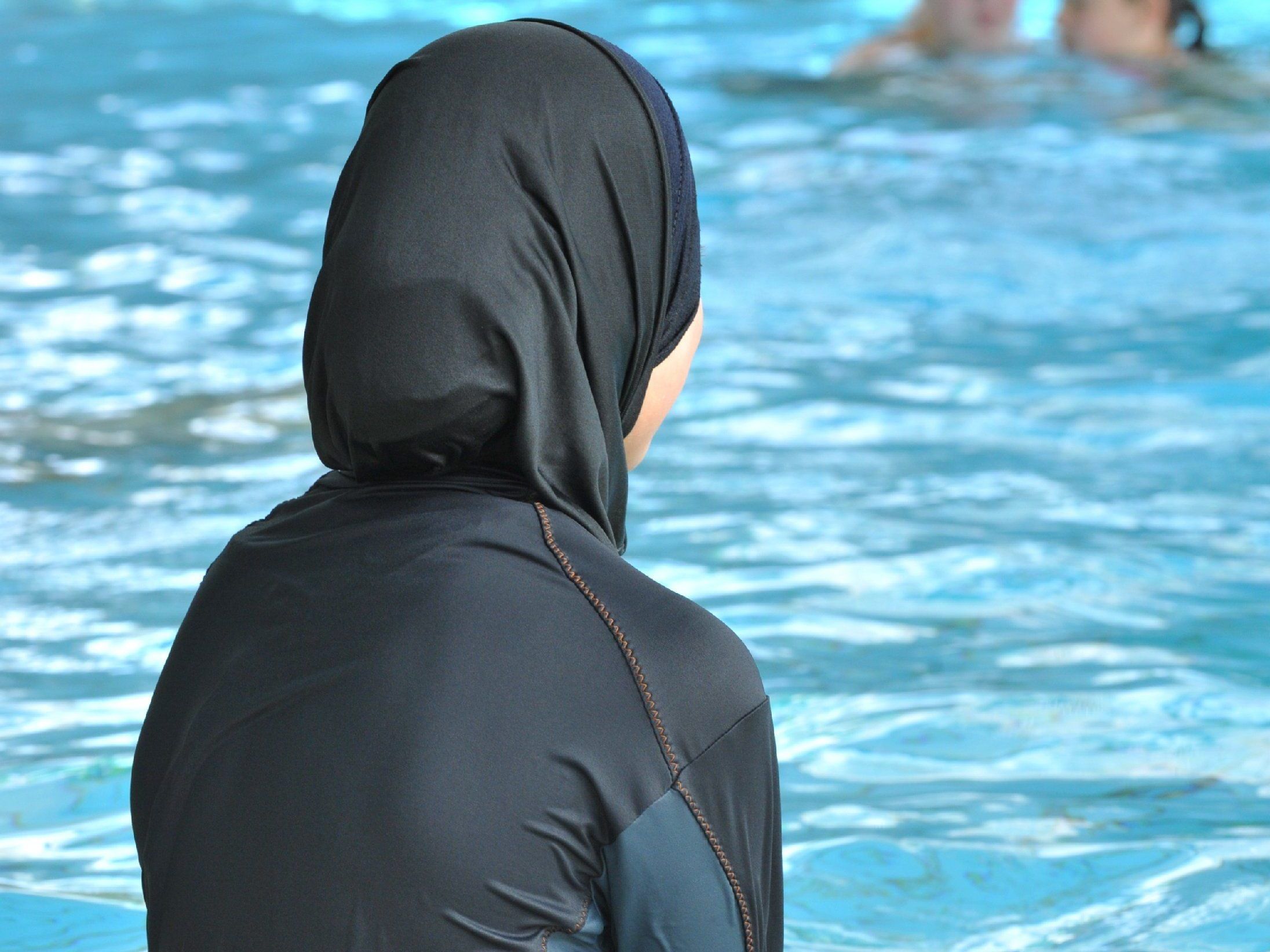 Eine muslimische Schülerin der Vigeliusschule in Freiburg sitzt in einem Ganzkörper-Badeanzug am Rande des Schwimmbeckens.