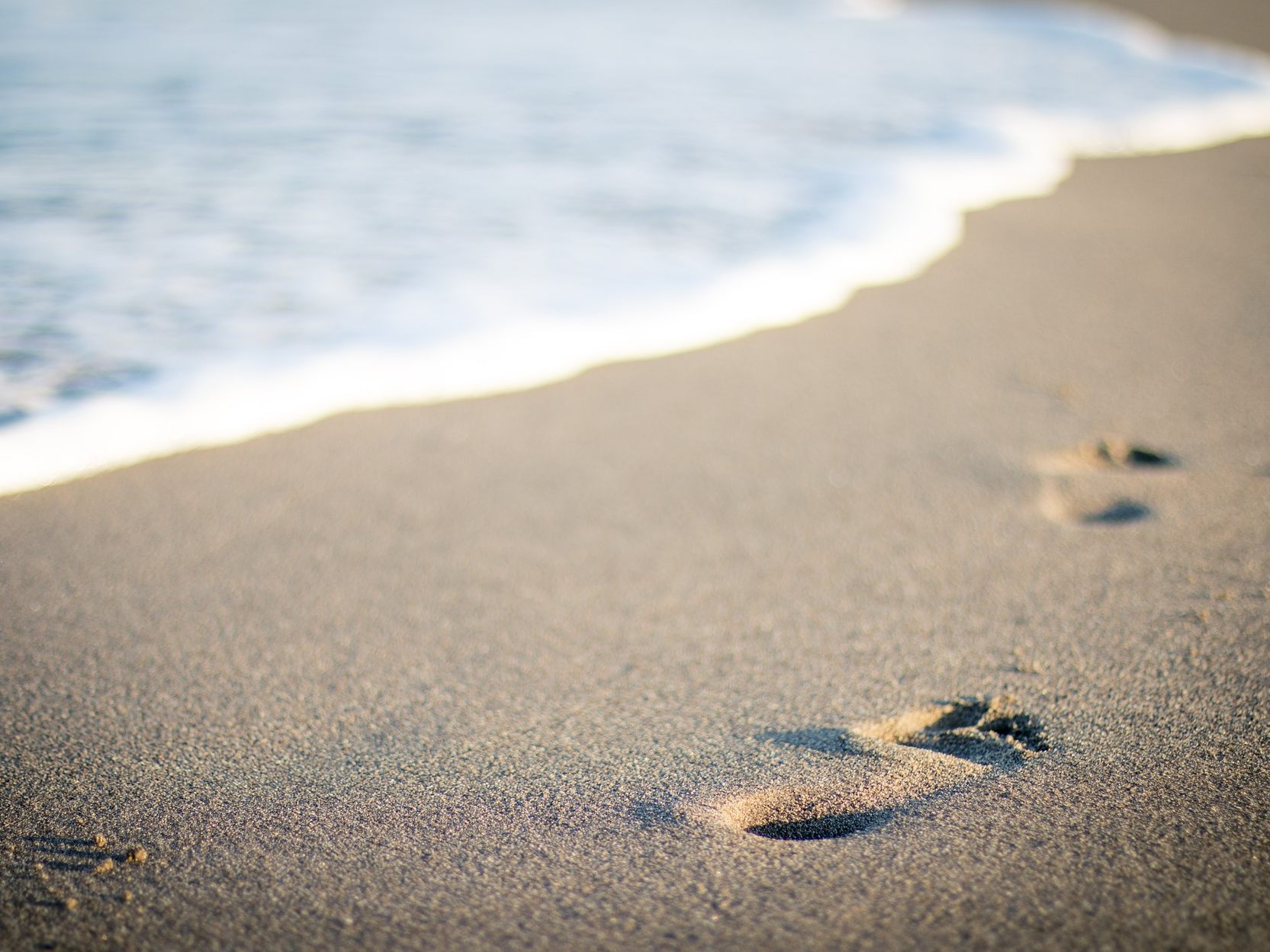 Symbolfoto eines Sandstrandes mit Fußabdrücken.