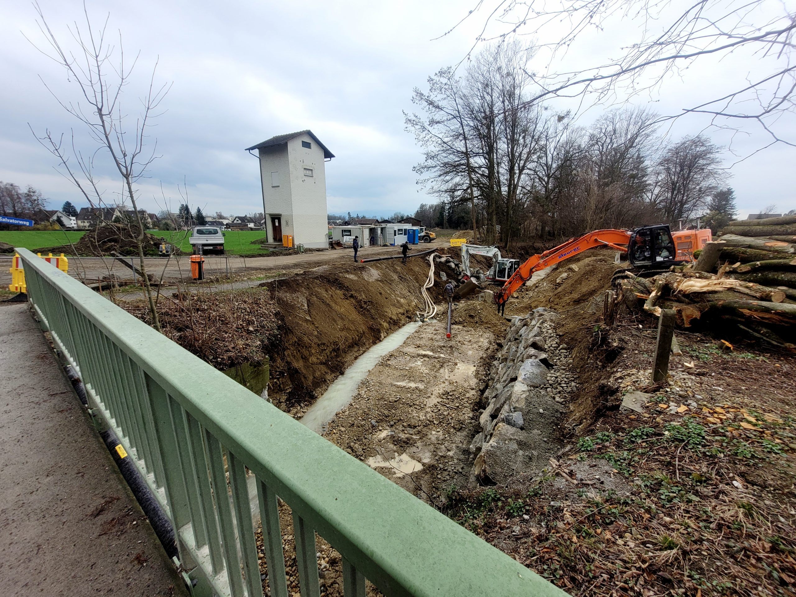 Blick von der Brücke L18 auf die Baustelle Hochwasserschutzprojekt Ruggbach: Prallufersicherung und Nachbettsicherung sowie aktuell die Verlegung der Stromleitung unter dem Ruggbach hindurch. Blick von der Brücke L18 auf die Baustelle Hochwasserschutzprojekt Ruggbach: Prallufersicherung und Nachbettsicherung sowie aktuell die Verlegung der Stromleitung unter dem Ruggbach hindurch.