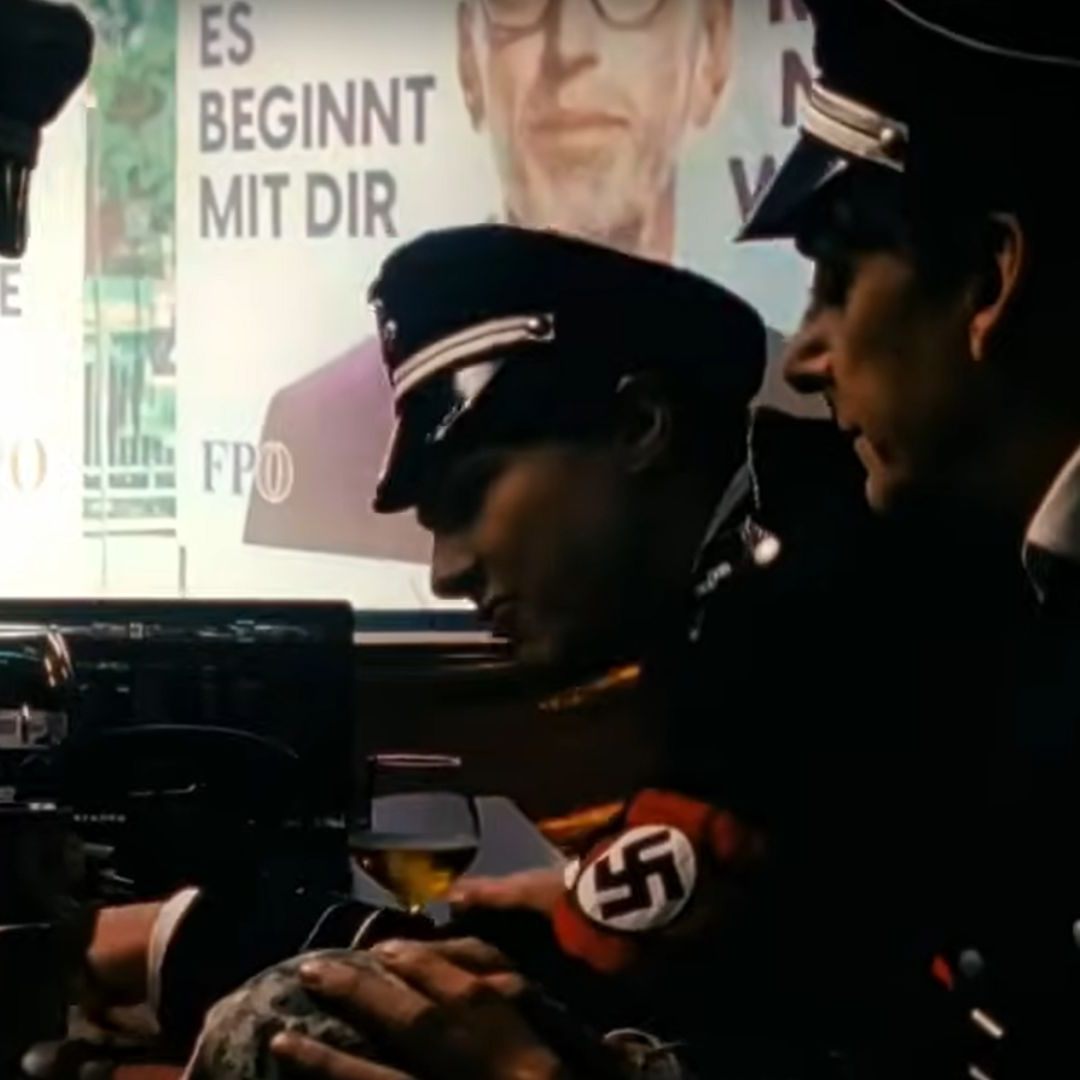 Die Performer sind in Uniformen mit Hakenkreuz-Binden und Hitler-Bart zu sehen.