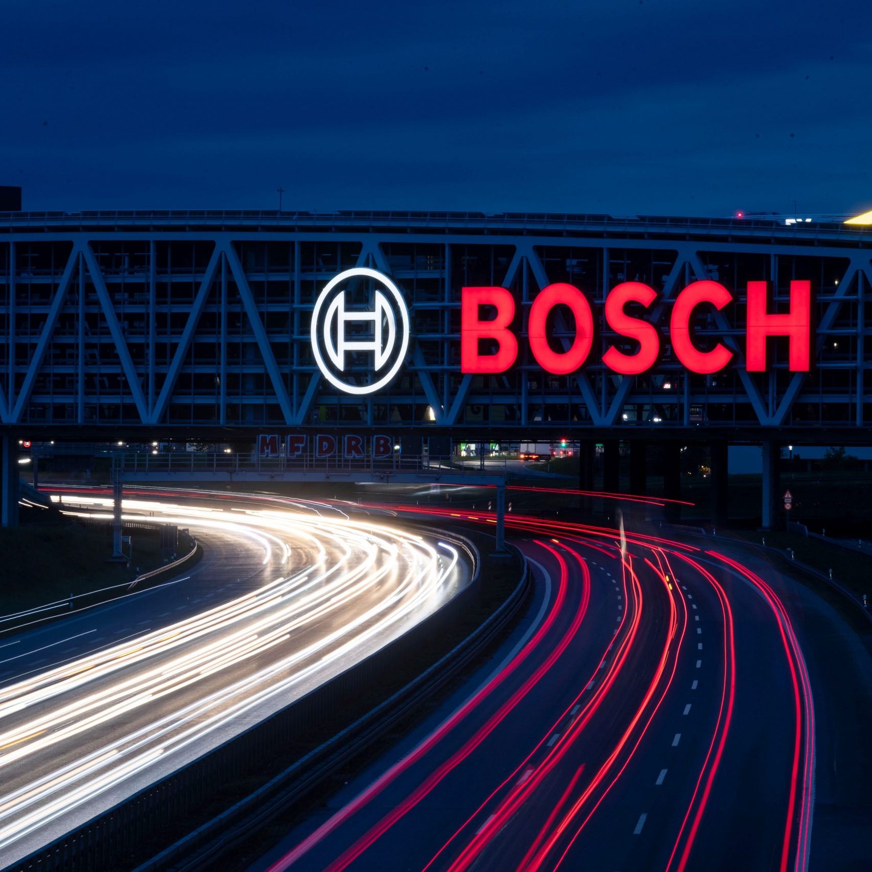 Das Logo des Technologiekonzerns Bosch leuchtet auf einem Parkhaus der Messe Stuttgart über der A8.