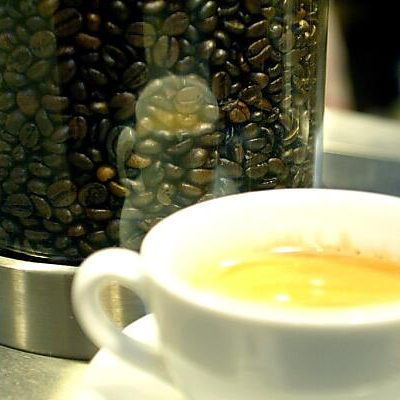 Frisch gebrühte Tasse Kaffee vor einem Behaelter mit Kaffeebohnen