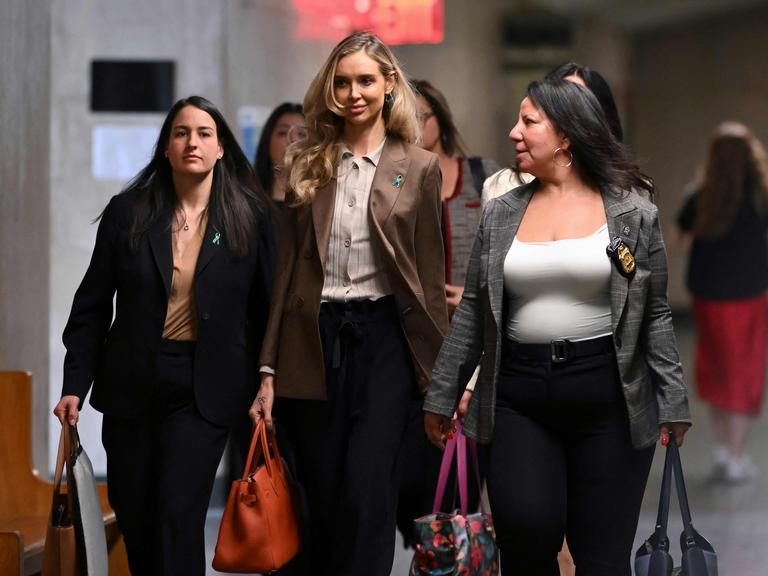 Katja Sokola (Mitte) betritt gemeinsam mit zwei Begleiterinnen ein Gerichtsgebäude. Sie trägt einen braunen Blazer und wirkt gefasst. Links und rechts gehen zwei Frauen mit ihr, eine davon in einem karierten Blazer mit Polizeimarke. Alle drei wirken entschlossen, während sie durch den Flur gehen. Im Hintergrund sind weitere Personen unscharf zu erkennen. Katja Sokola (Mitte) betritt gemeinsam mit zwei Begleiterinnen ein Gerichtsgebäude. Sie trägt einen braunen Blazer und wirkt gefasst. Links und rechts gehen zwei Frauen mit ihr, eine davon in einem karierten Blazer mit Polizeimarke. Alle drei wirken entschlossen, während sie durch den Flur gehen. Im Hintergrund sind weitere Personen unscharf zu erkennen.