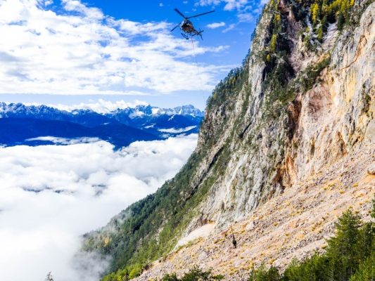 Auf dem Bild sieht man einen Hubschrauber an dem Berg entlangfliegen. Auf dem Bild sieht man einen Hubschrauber an dem Berg entlangfliegen.
