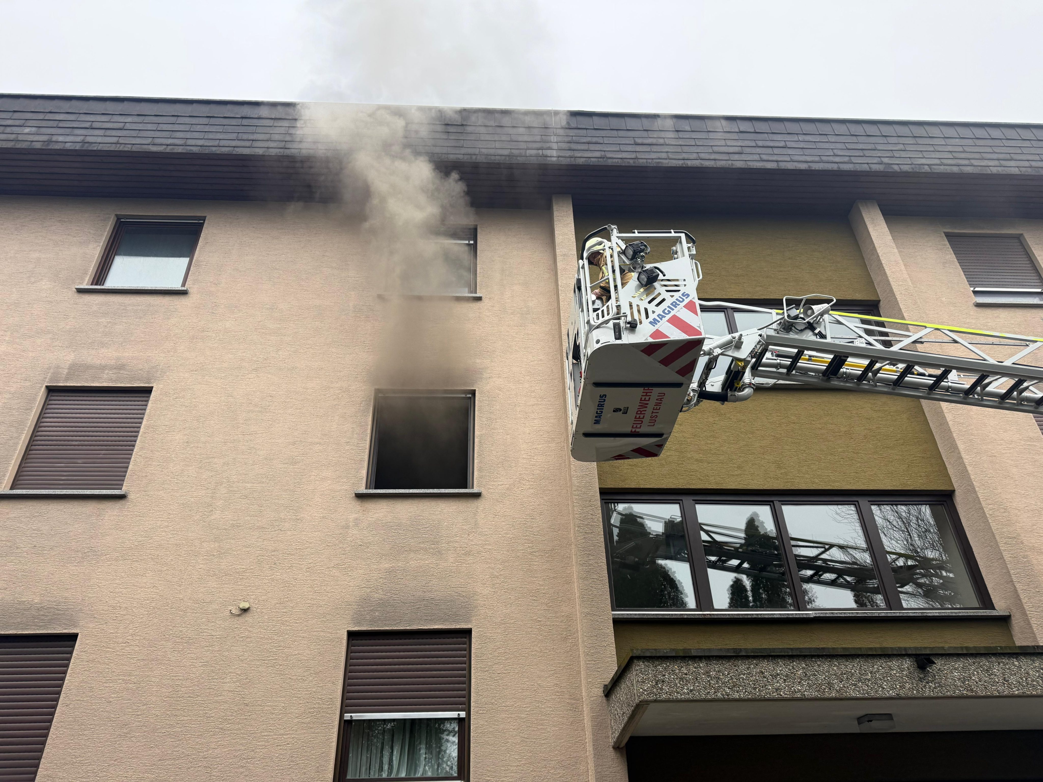 Dichter Rauch dringt aus einem Fenster im oberen Stockwerk der Wohnanlage. Die Feuerwehr bekämpfte den Brand von außen über eine Drehleiter.